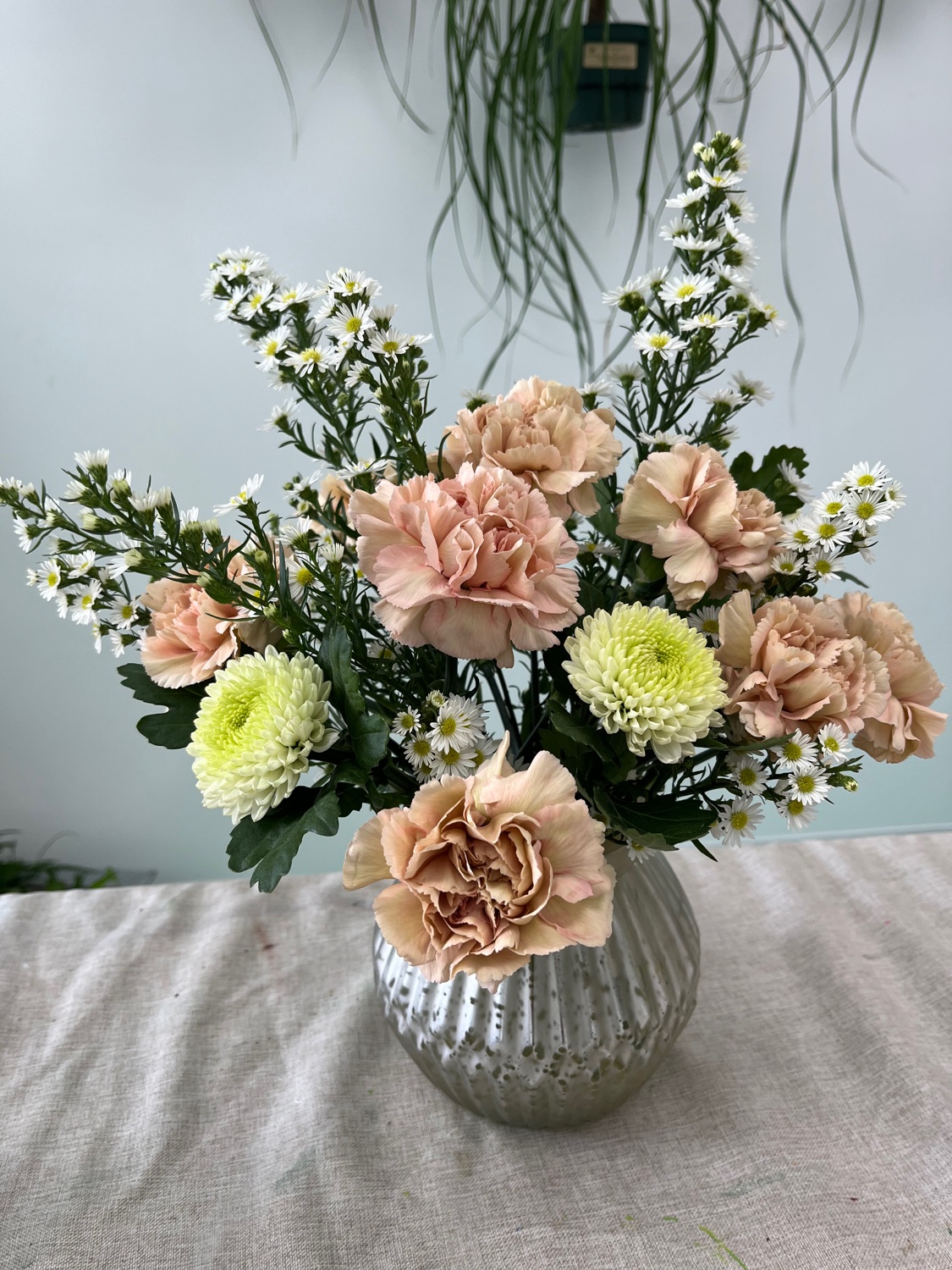 Large weekly bouquet in a silver vase with peach carnations, pale green mums, and white daisies