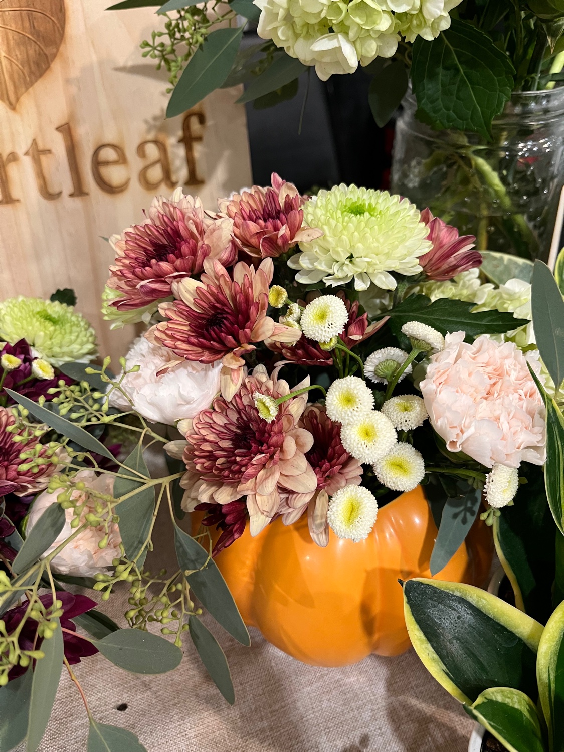 Seasonal arrangement in an orange pumpkin vase with burgundy and cream mums, peach carnations, and eucalyptus